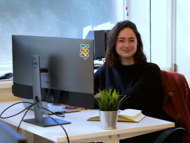 Woman in sitting in front of the computer with Amberscript logo attached to the back of the display